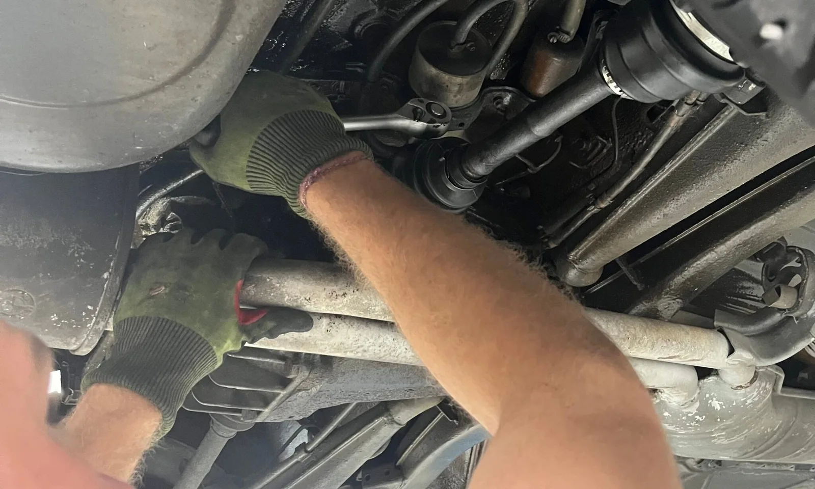 Mechaniker mit Arbeitshandschuhen und Ratsche an der Hinterachse eines aufgebockten Fahrzeugs